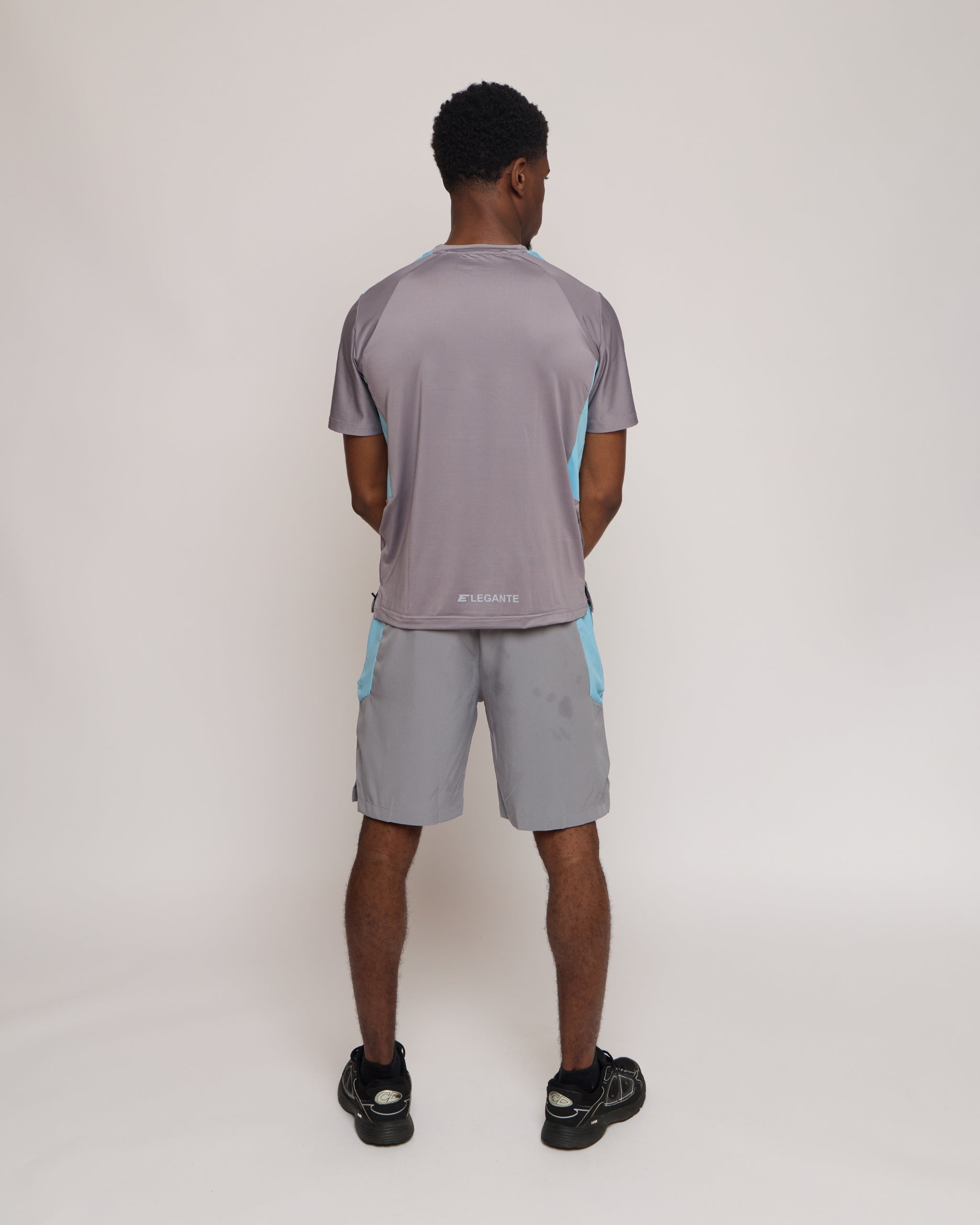 Man wearing a gray athletic shorts and t-shirt outfit with blue accents on a white background