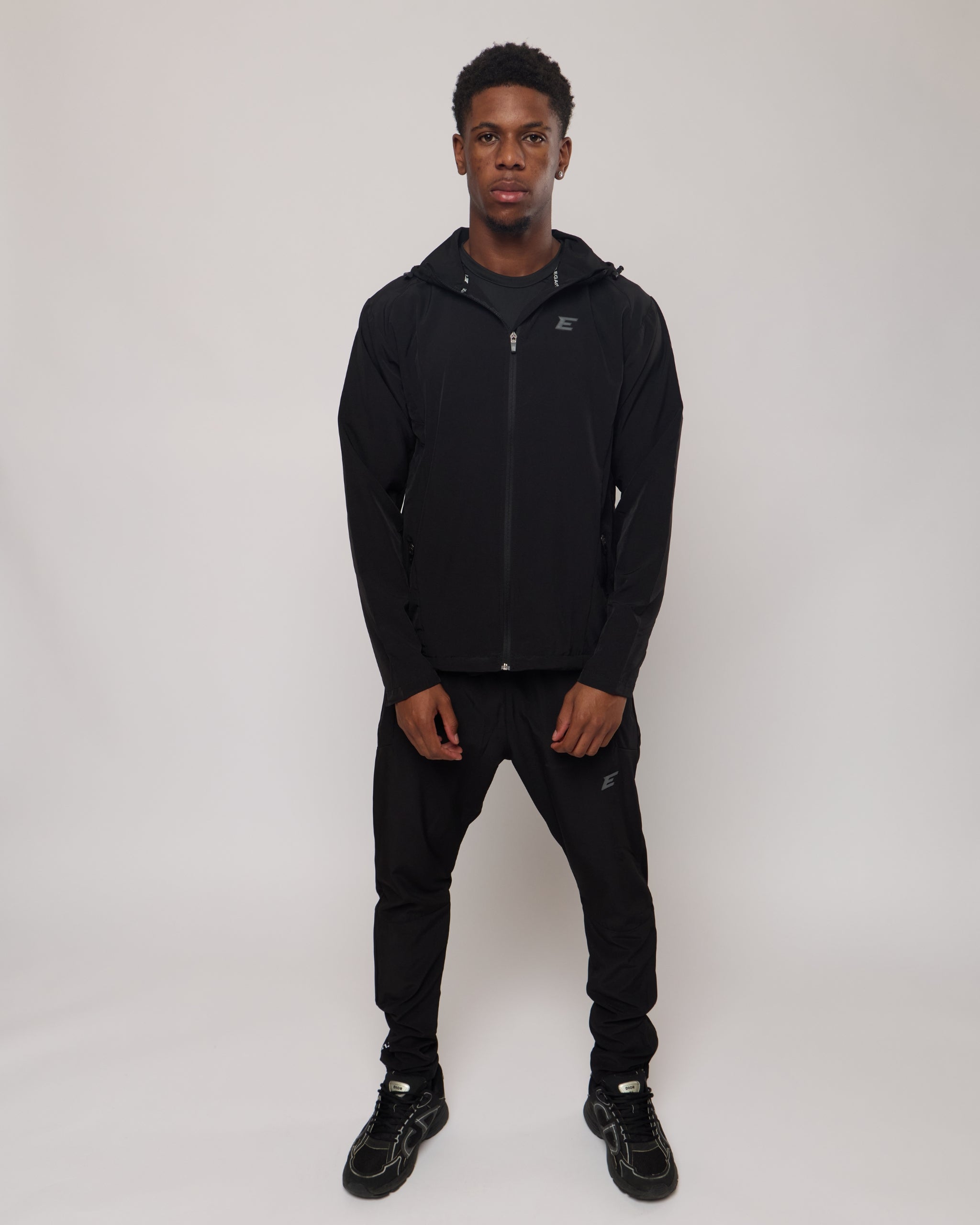 man wearing a black tracksuit hoodie and tracksuit pants on a white background