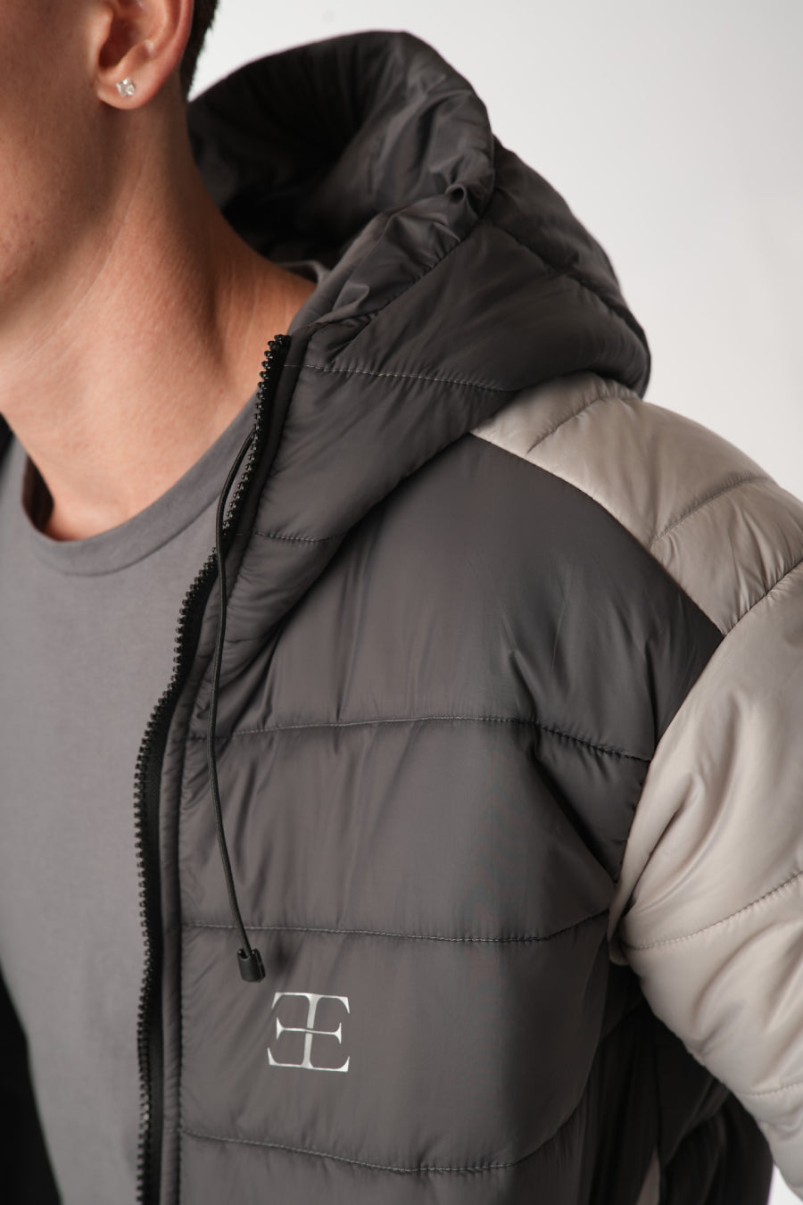 Close-up of a man wearing a black grey puffer vest with elegante brand logo on a neutral background