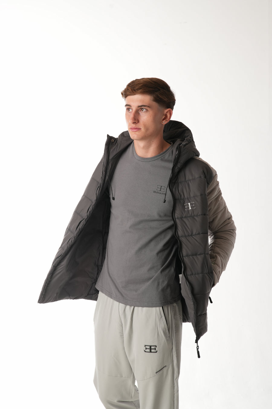 Man wearing a dark gray jacket over a gray shirt with light gray pants on a white background