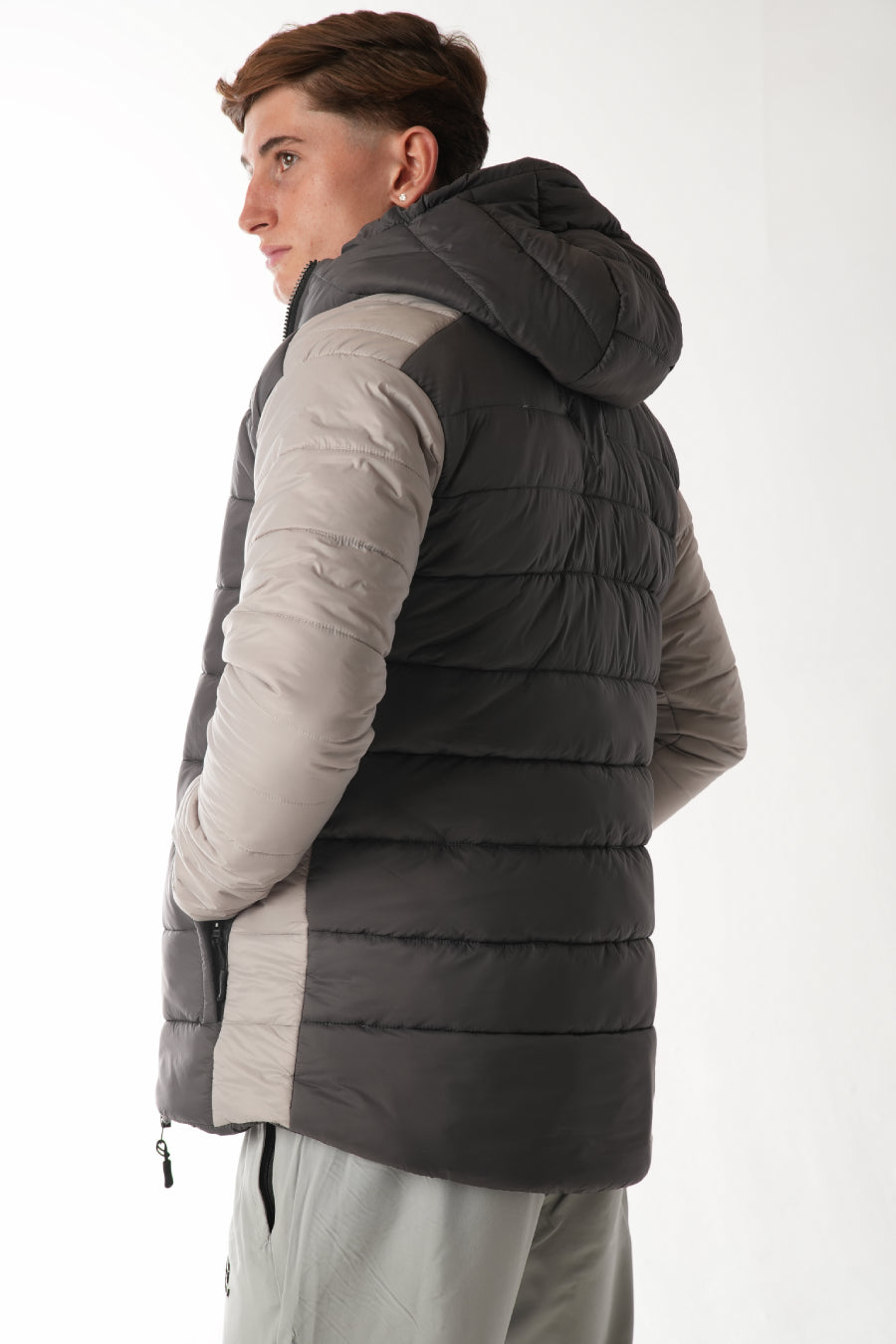 Person wearing a gray puffer vest over a beige long-sleeve shirt on a white background