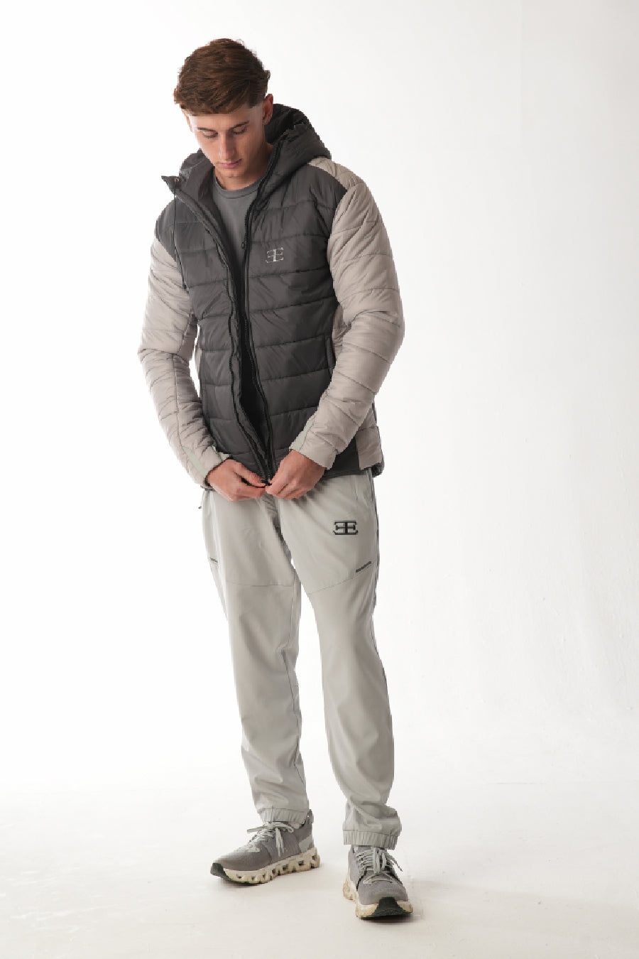 Man wearing a gray and black puffer elegante brand  vest over a gray hoodie and pants on a white background