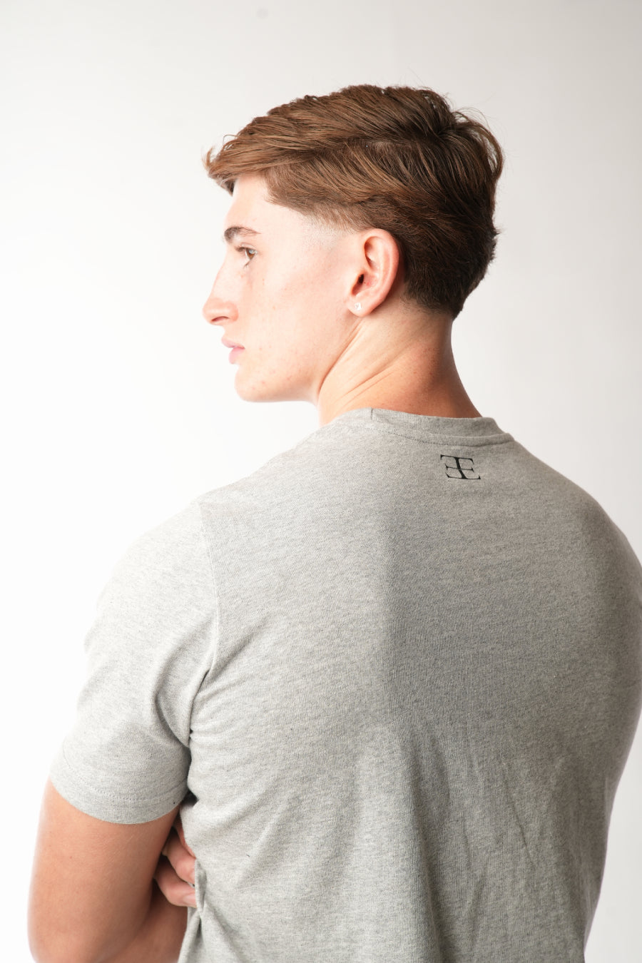 Person wearing a gray t-shirt with a logo on the back against a white background