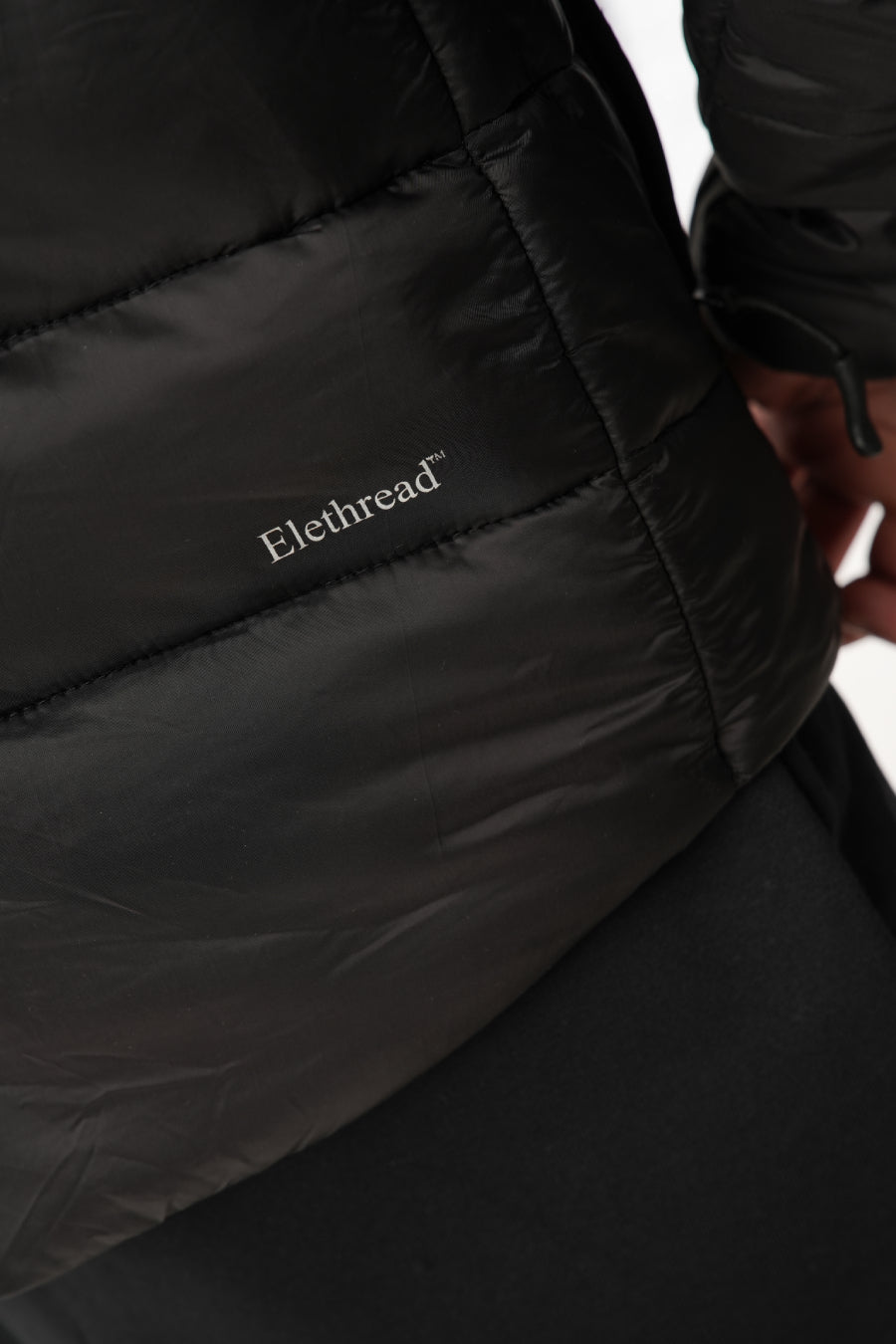 Close-up of a black jacket with 'Elethread' branding on a white background