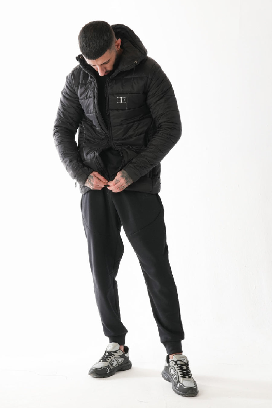 Man wearing a black puffer jacket and pants on a white background