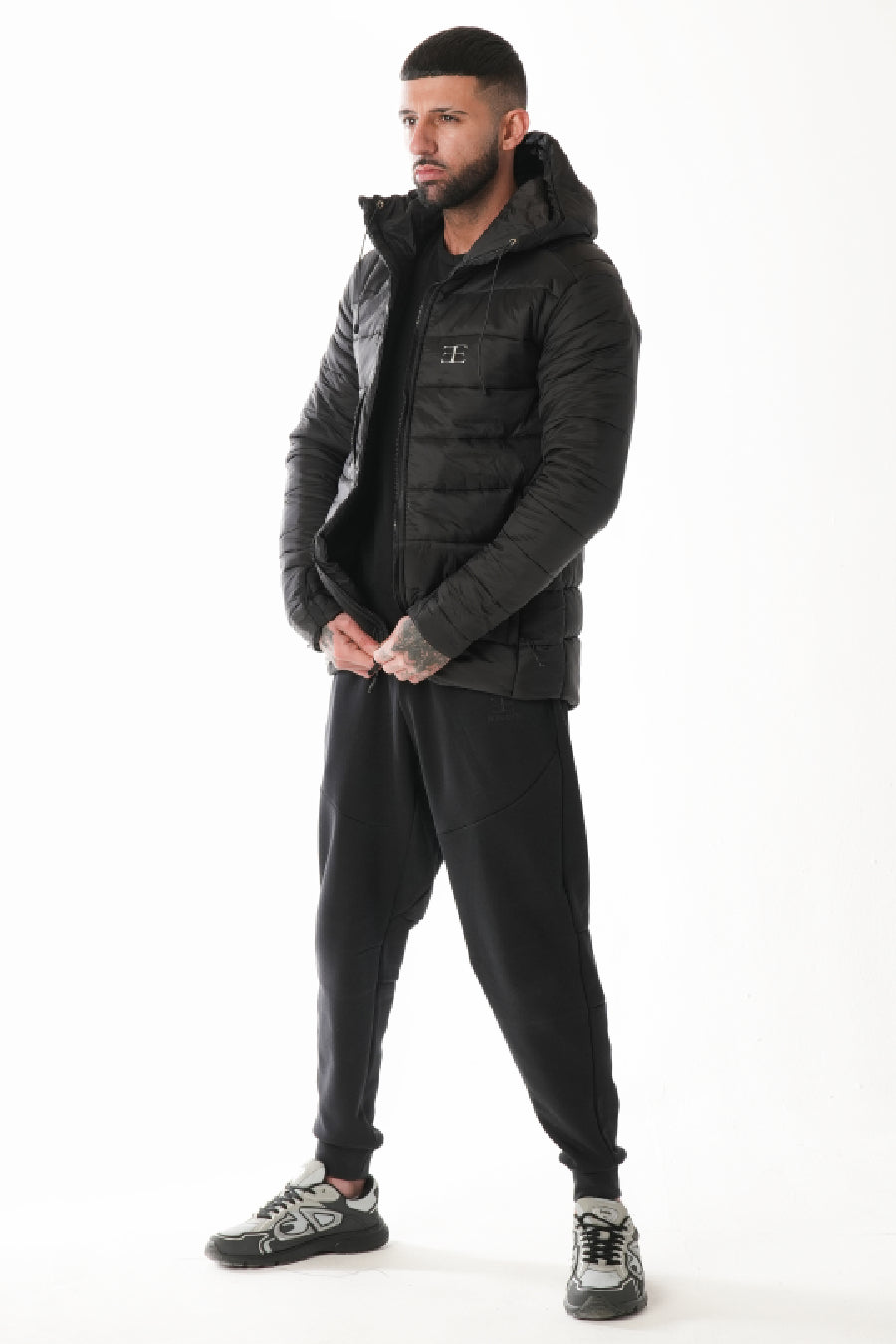 Man wearing a black puffer jacket and pants on a white background