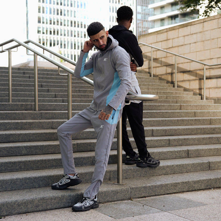 two men wearing sports tracksuits on city stairs one man wearing a grey and light blue tracksuit set and another man wearing a black and grey tracksuit set