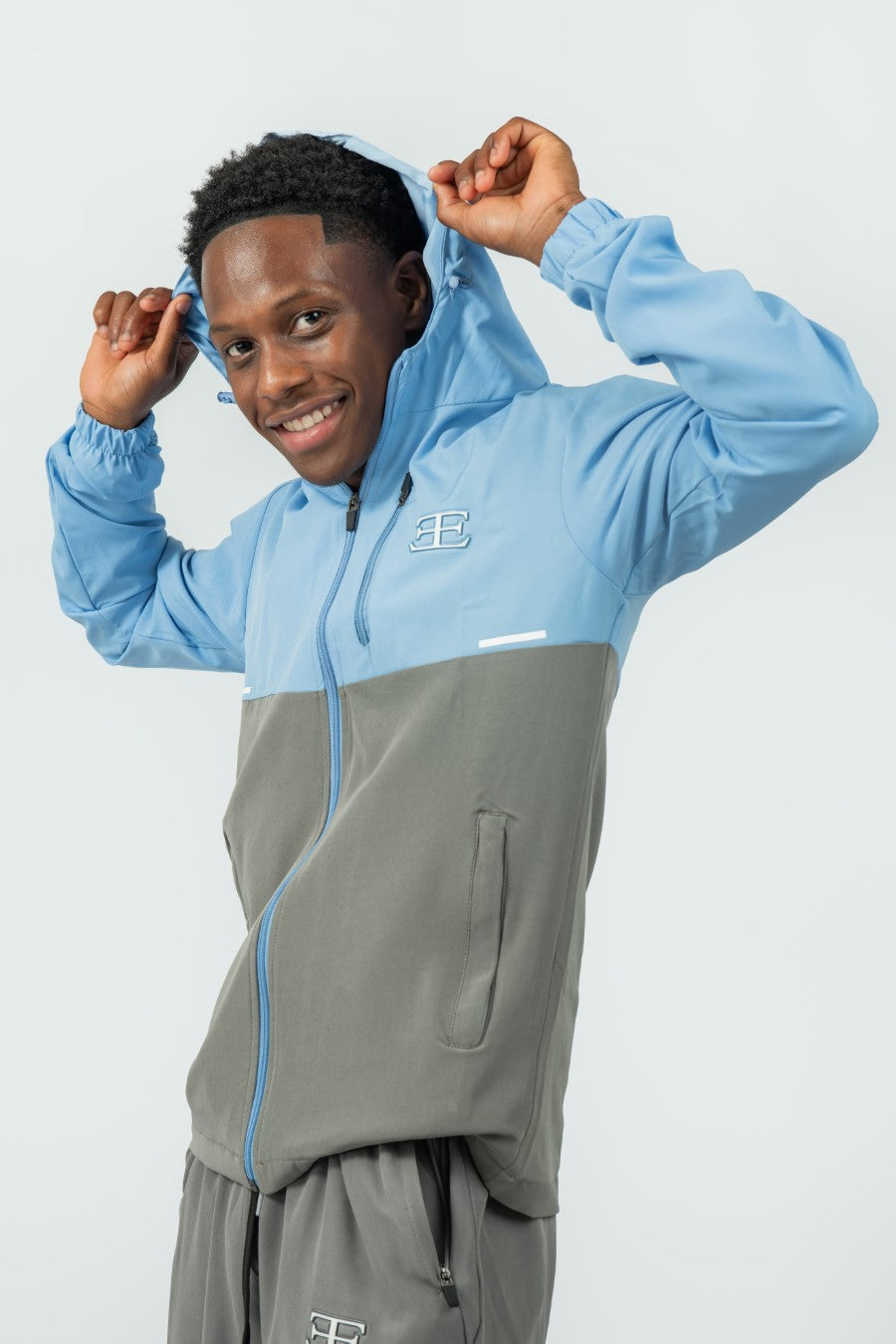 man wearing a two-tone blue and gray jacket holding the hood with a elegante brand logo on a white background