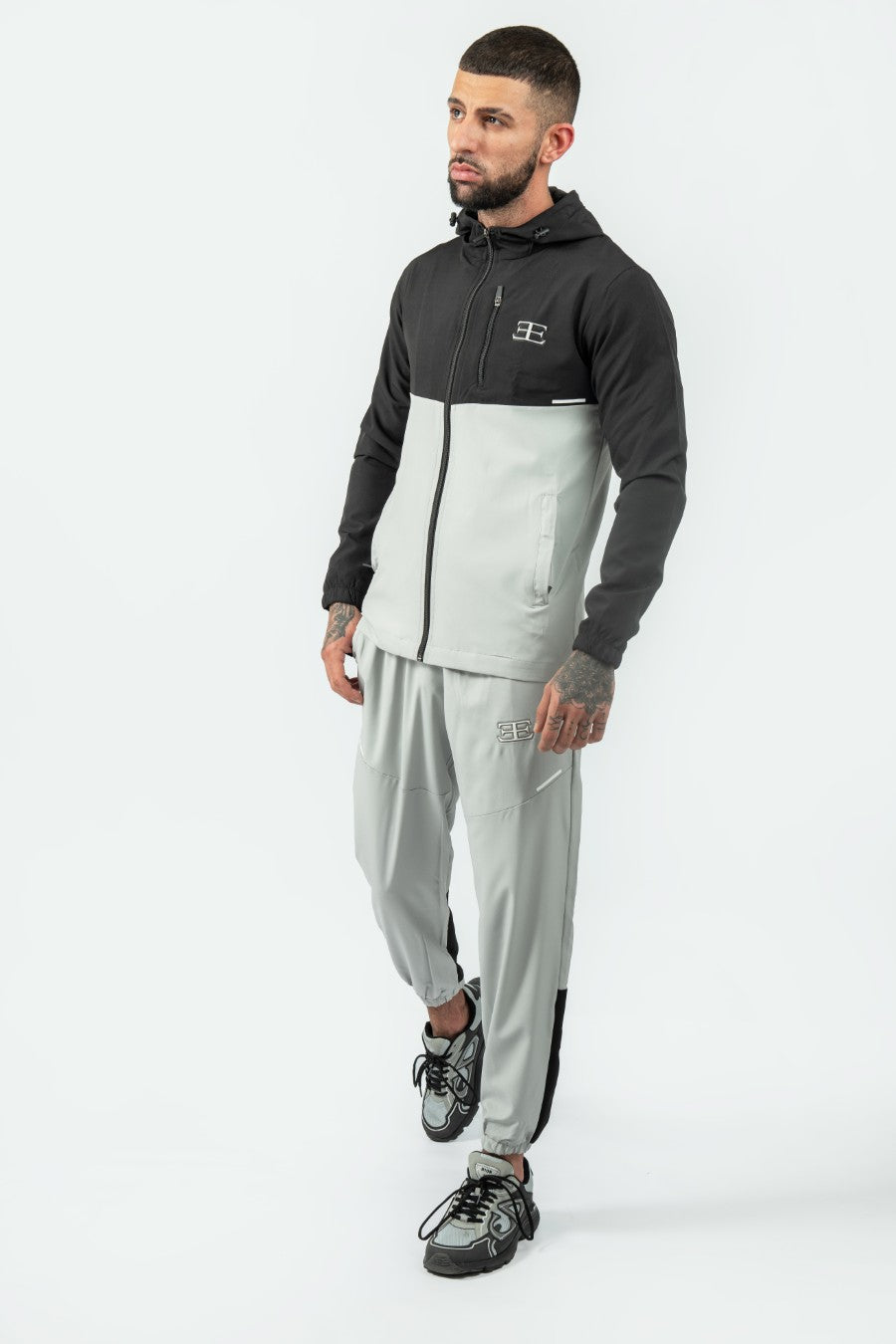 man wearing a gray and black tracksuit jacket and joggers on a white background
