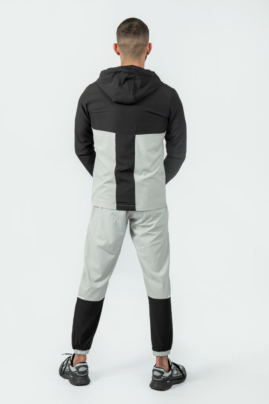 man wearing a gray and black tracksuit jacket and joggers on a white background