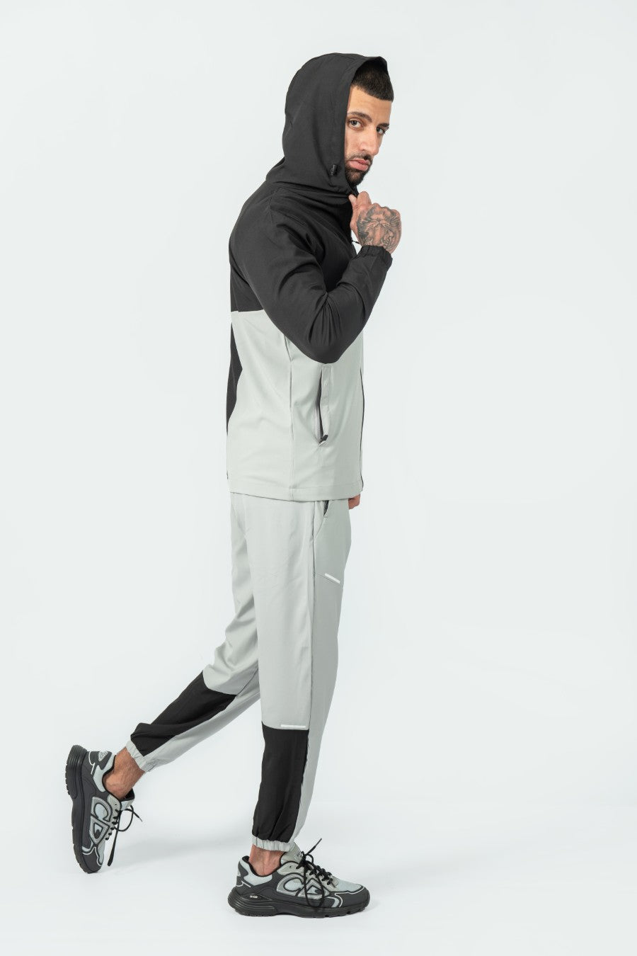 man wearing a gray and black tracksuit jacket and joggers on a white background