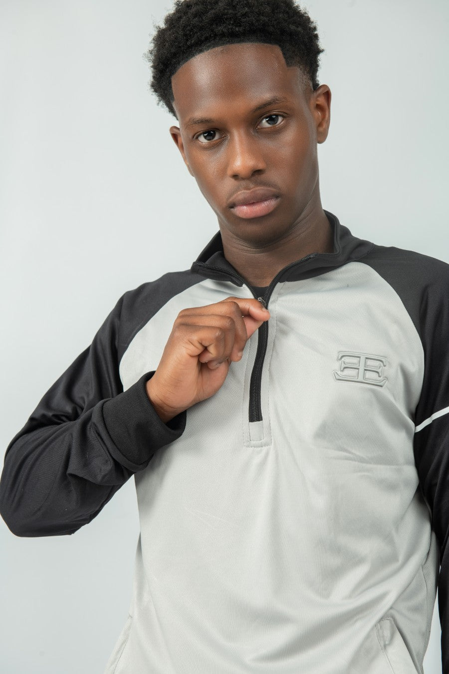 man wearing a black and gray sports zip top with elegante brand logo on a light gray background