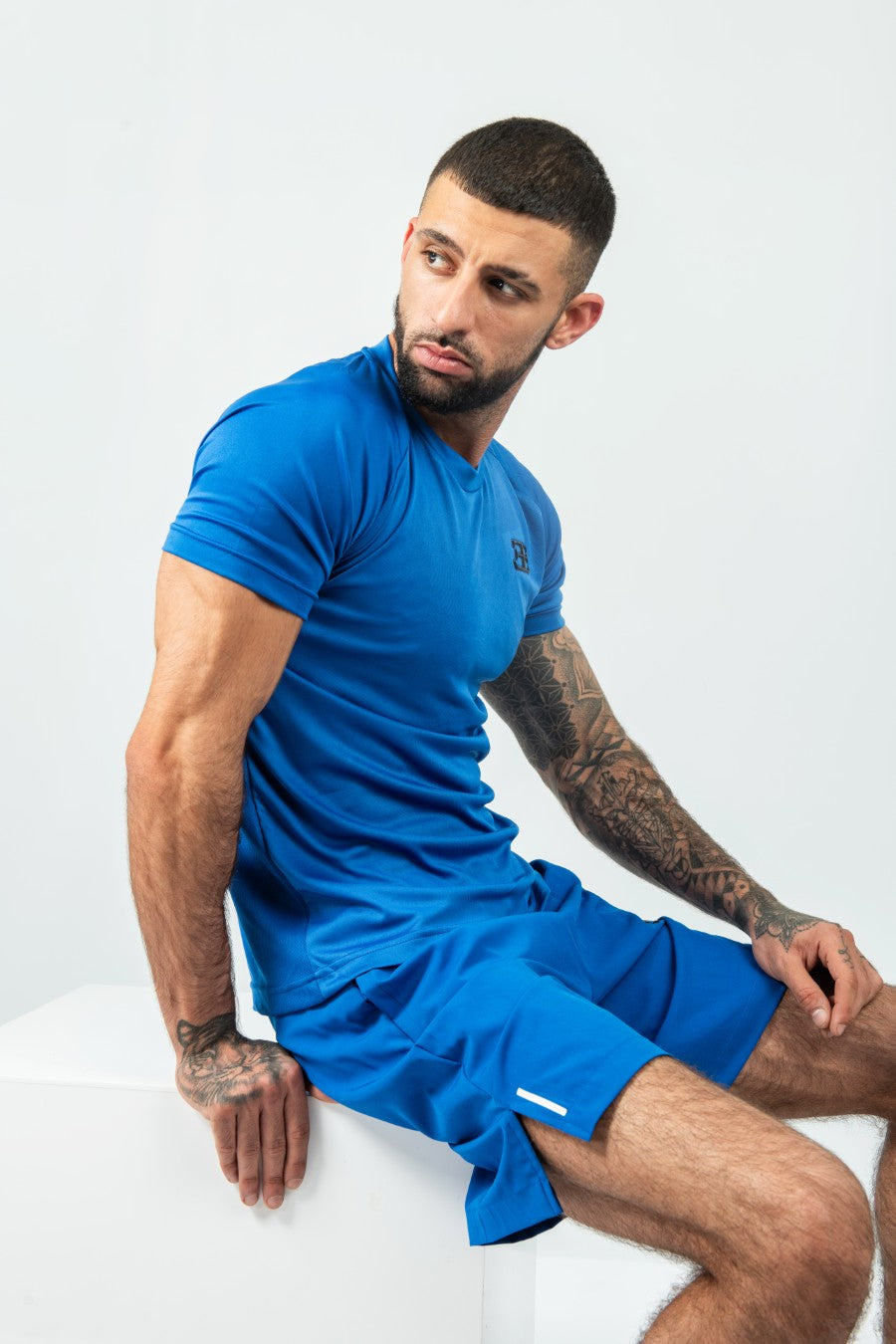 Man wearing a blue matching athletic shorts and tshirt sitting on a white surface with a plain background