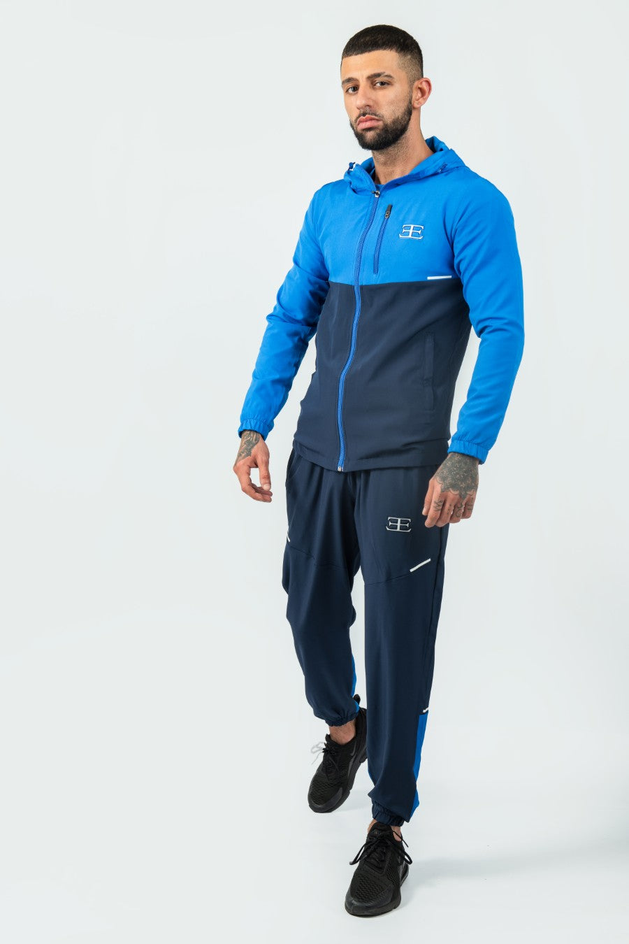 Man wearing a blue and navy tracksuit jacket and joggers set on a white background
