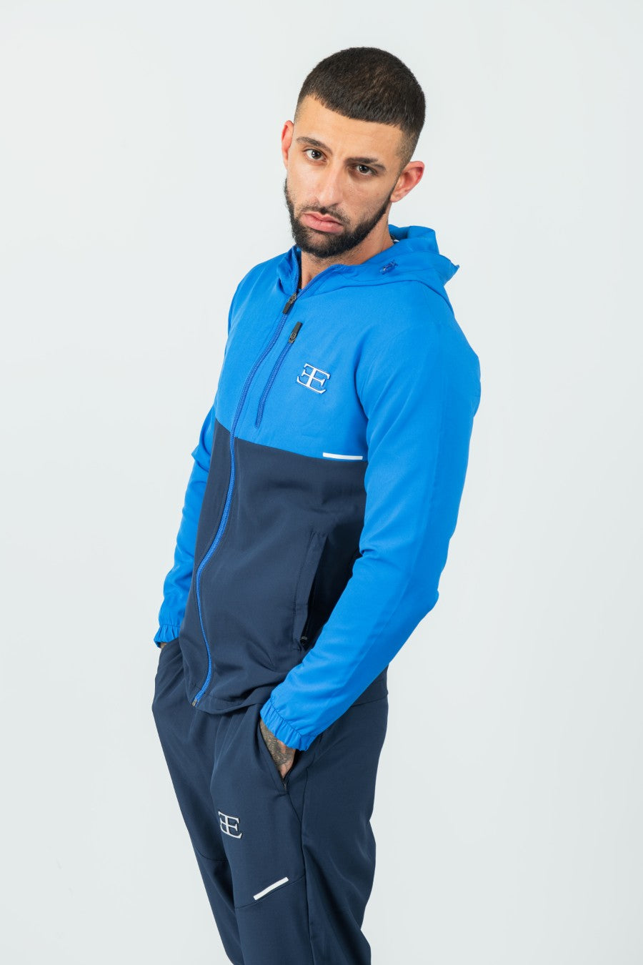 Man wearing a blue and navy tracksuit jacket and joggers set on a white background