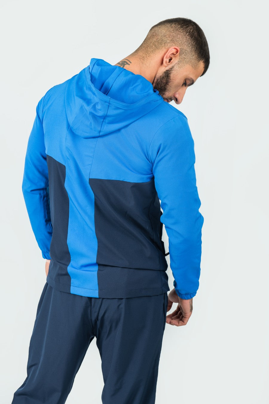 man wearing a blue and navy tracksuit jacket and joggers with hood on a white background