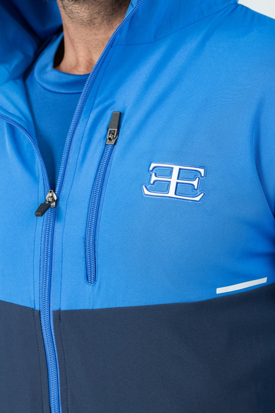 close up of Man wearing a blue and navy tracksuit jacket with zip and elegante logo 