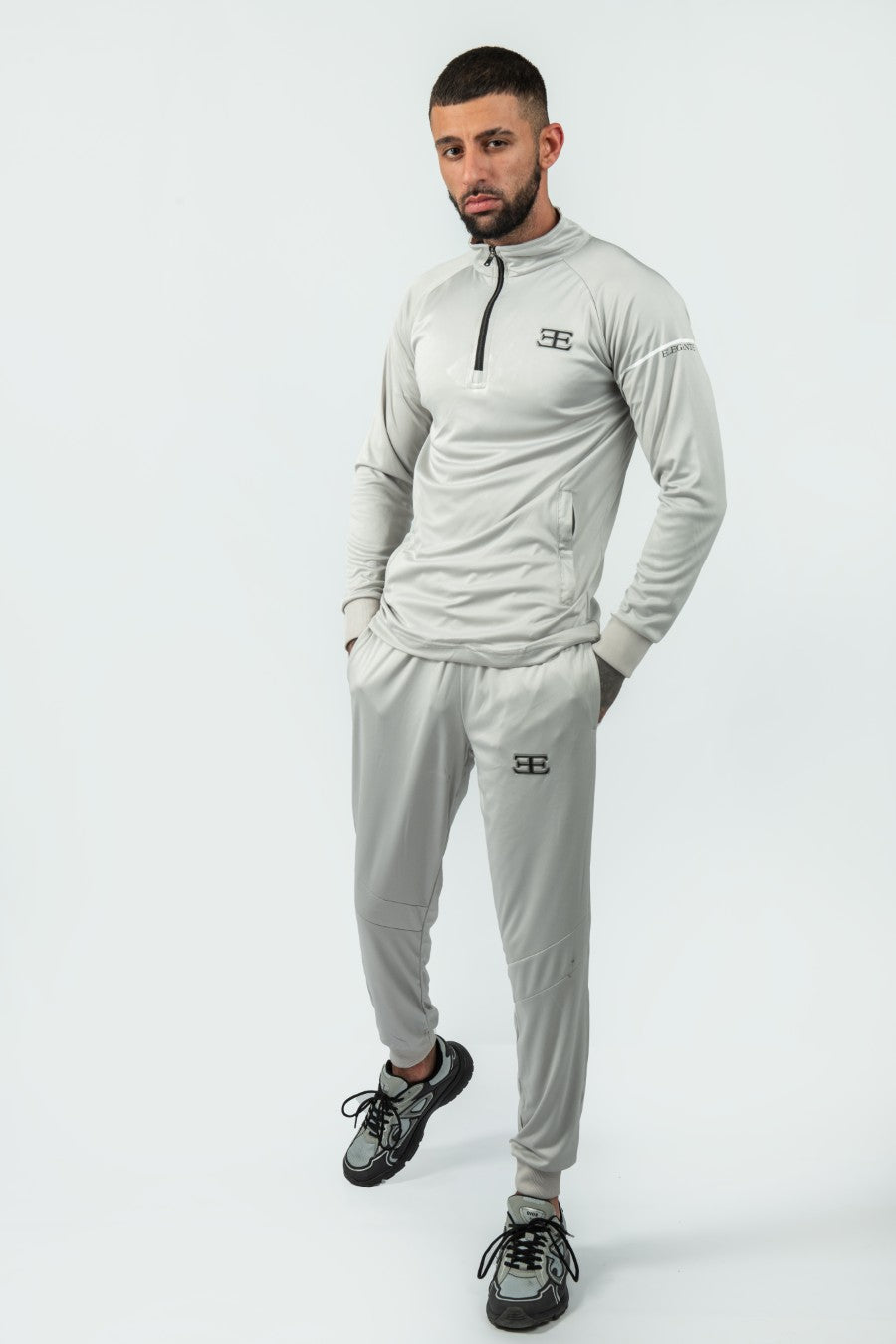 Man wearing a gray tracksuit top and joggers with elegante brand logo on a white background