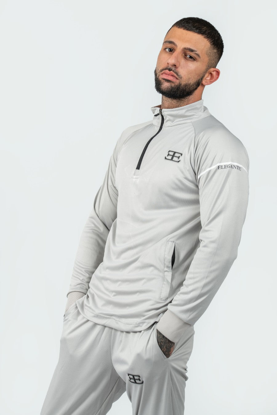 Man wearing a full light gray tracksuit with a brand logo on a white background