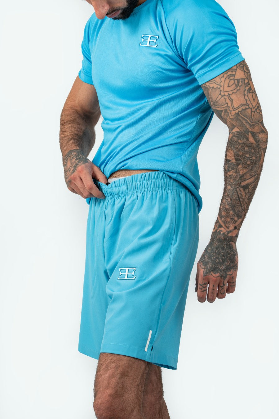man wearing a matching blue athletic shorts and tshirt outfit with elegante logo on a white background