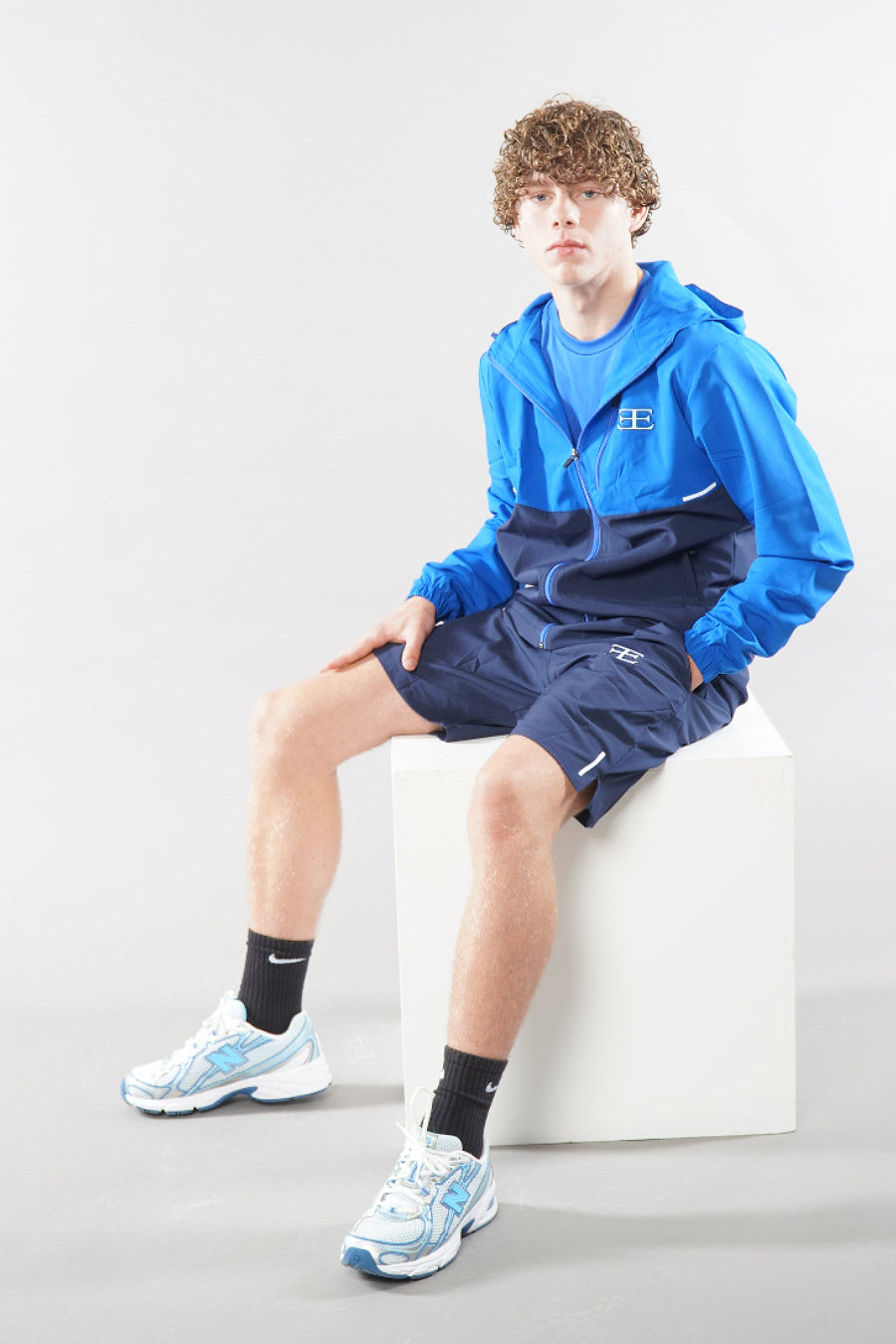 Man wearing a blue tracksuit jacket with shorts with a logo on a white background