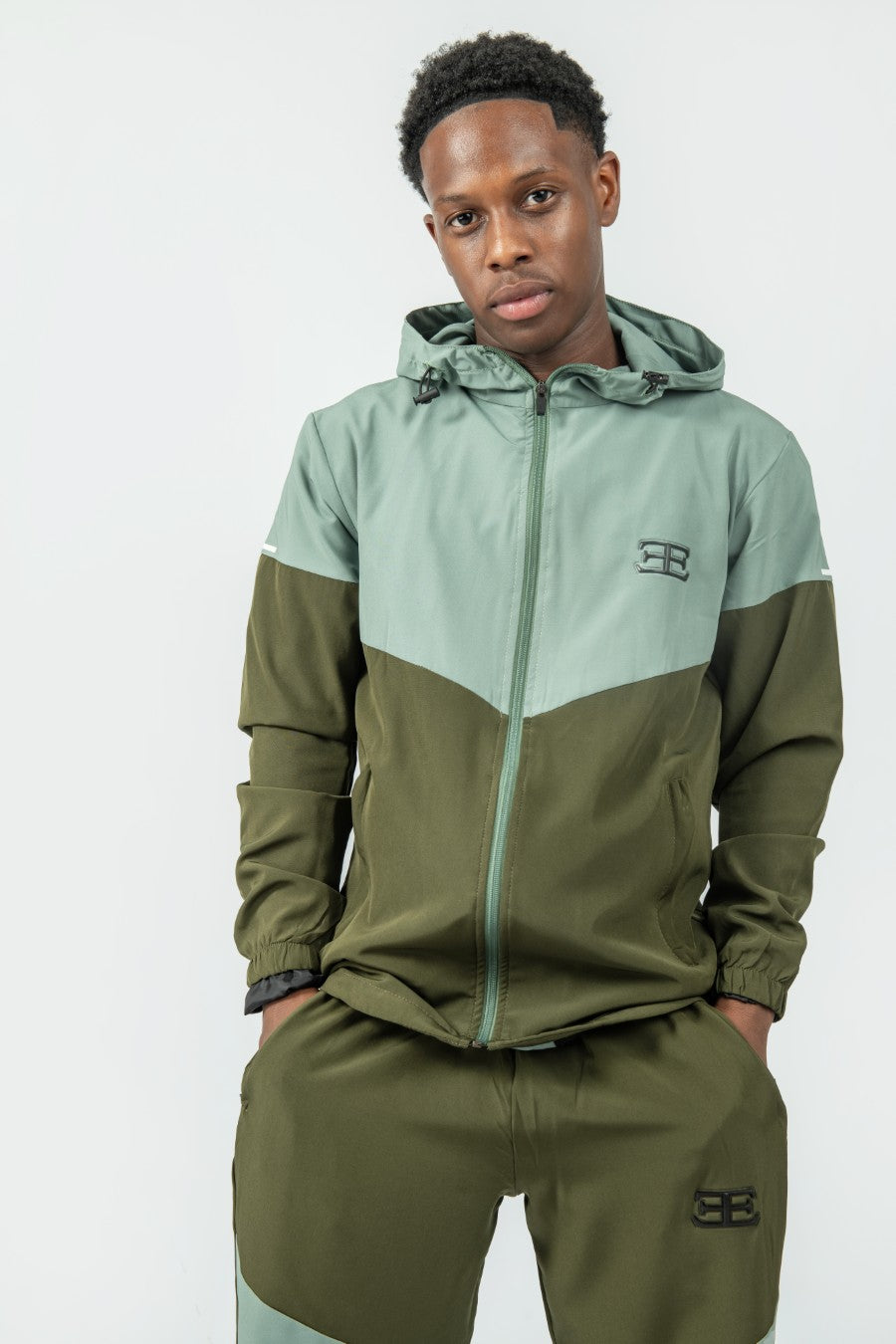 Person wearing a green and light gray tracksuit with a brand logo on a white background