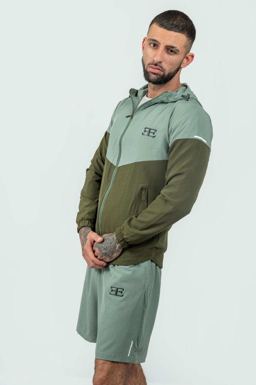 Man wearing a green and olive tracksuit with a logo on a white background