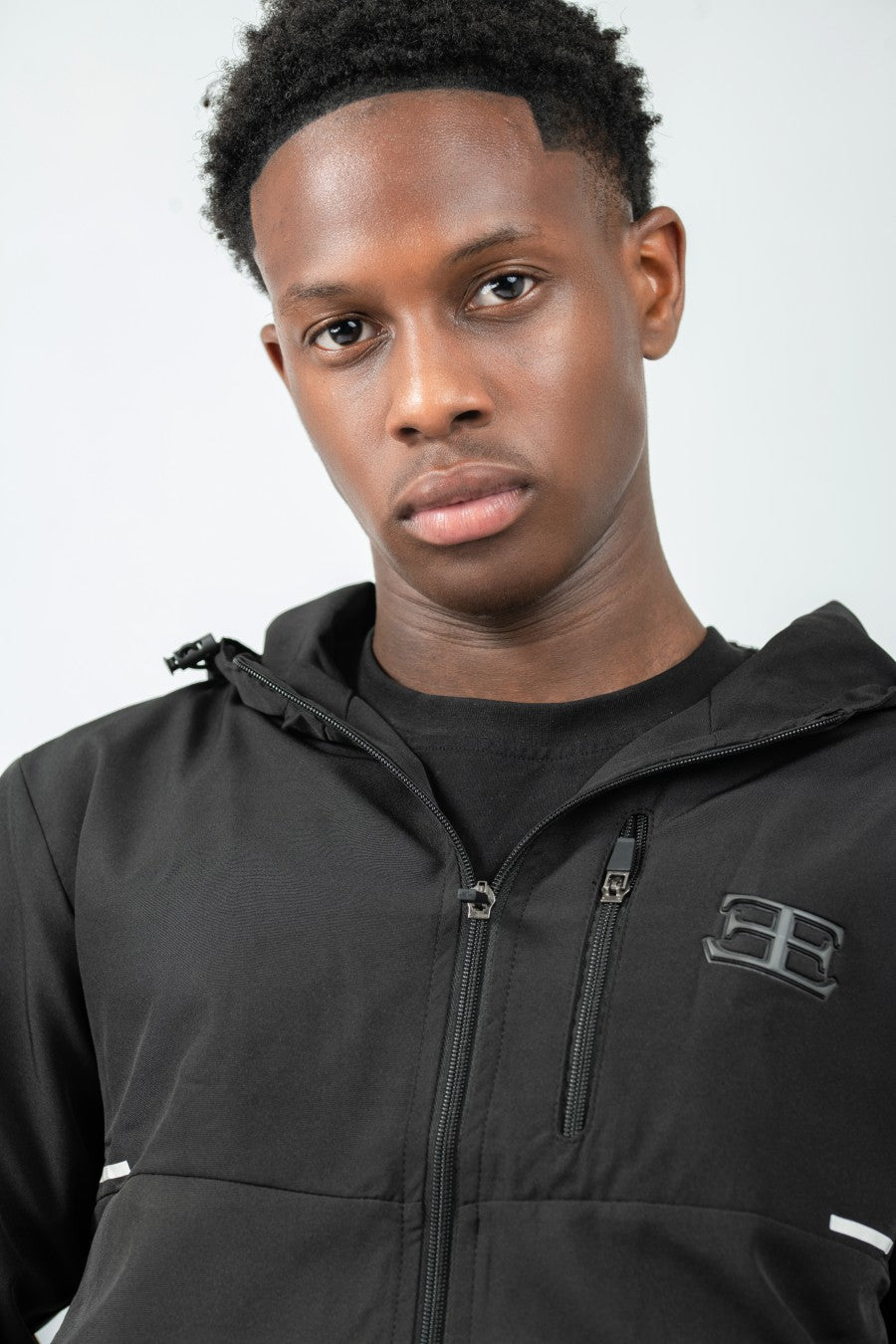 Man wearing a black jacket with a brand logo on a white background