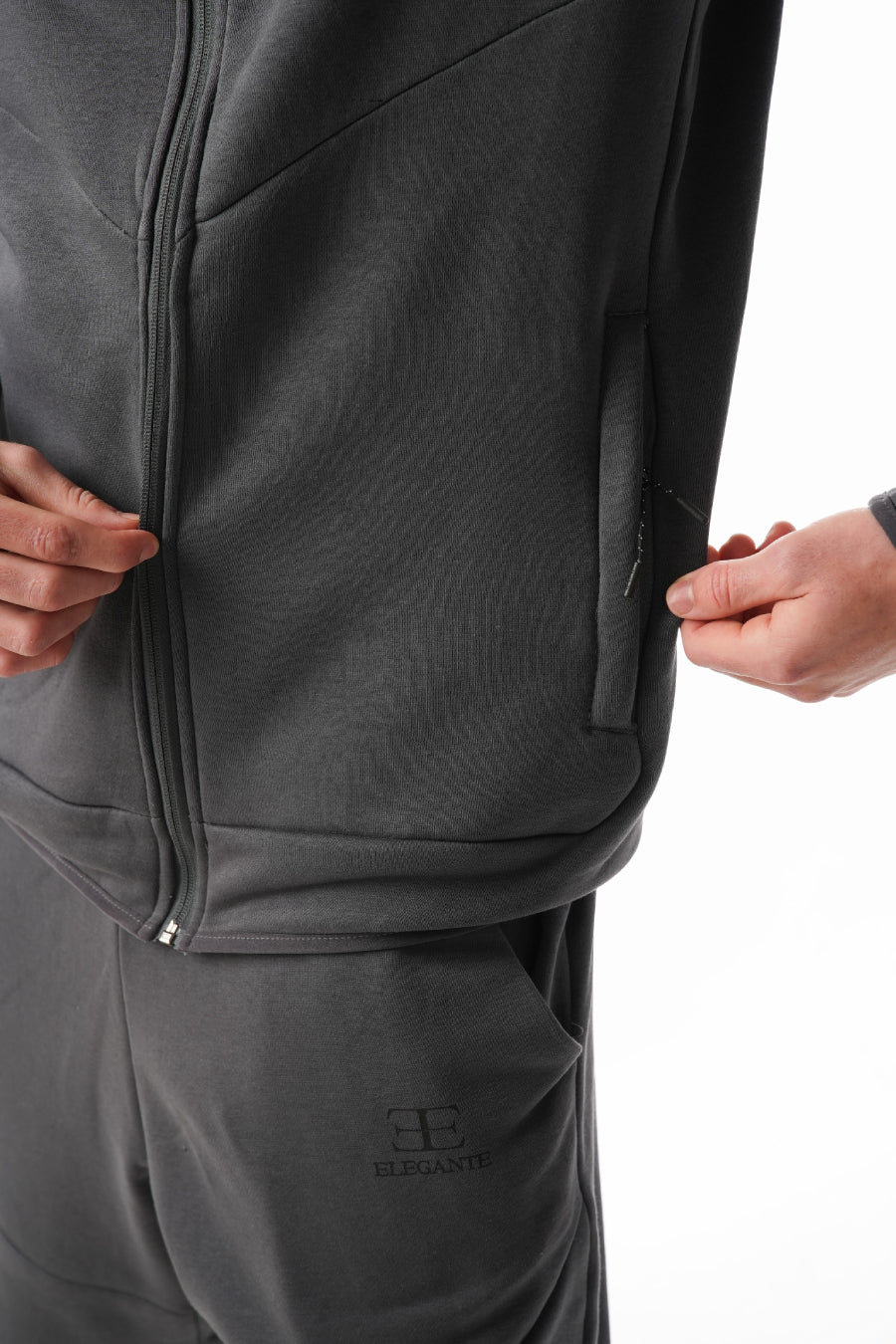 Close-up of a person wearing a dark gray tracksuit with a brand logo on a white background