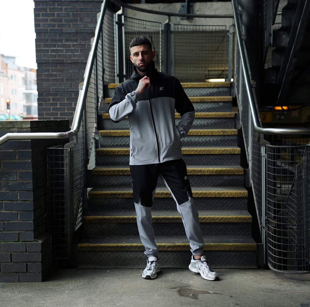 man wearing grey and black tracksuit joggers and jacket with a staircase in the background