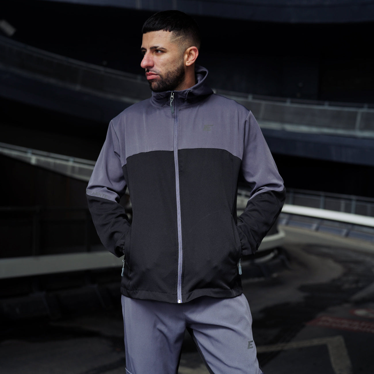 Man wearing a black and grey tracksuit jacket with hood and pants in an urban setting