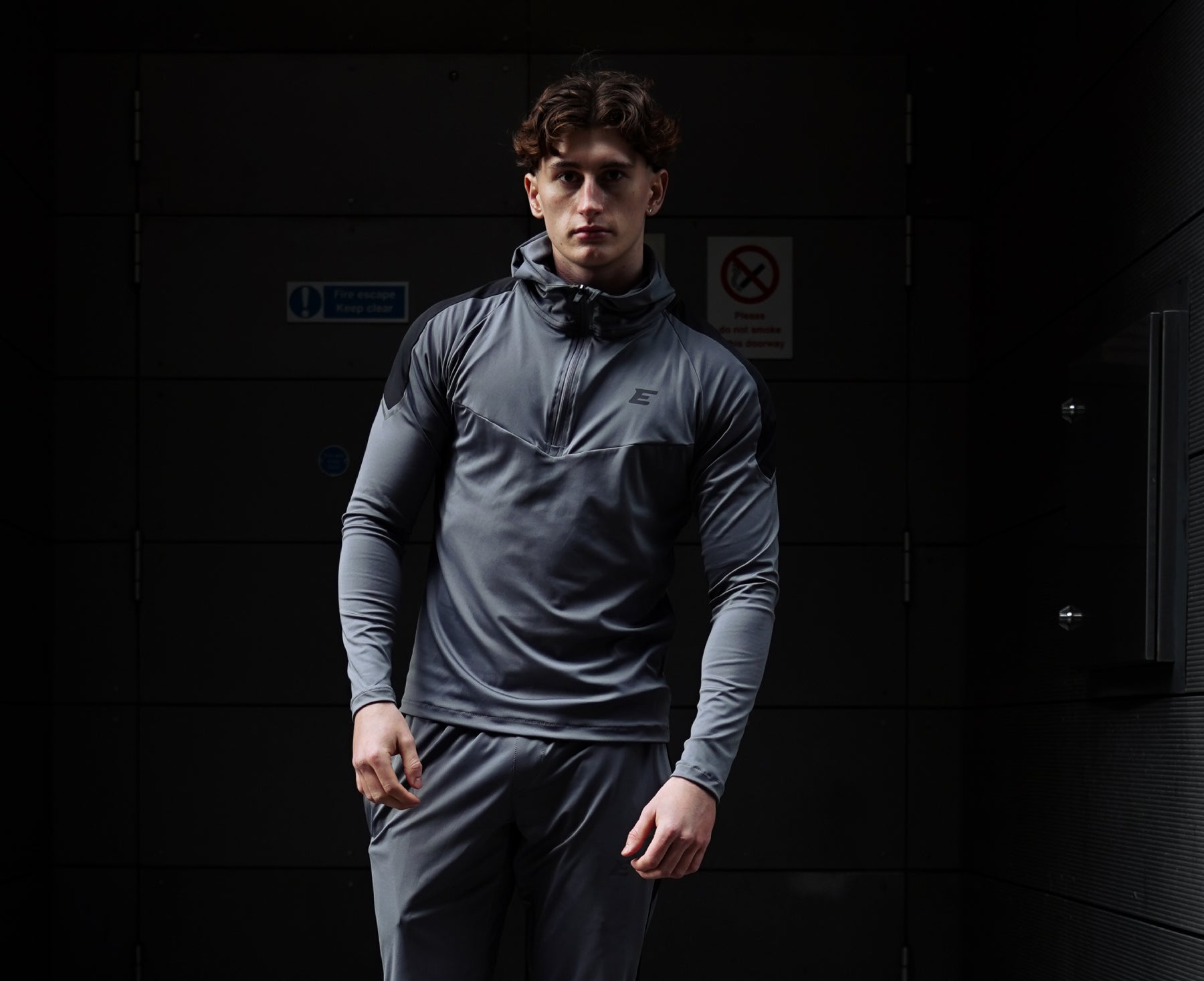 Man wearing a gray athletic outfit standing against a dark background