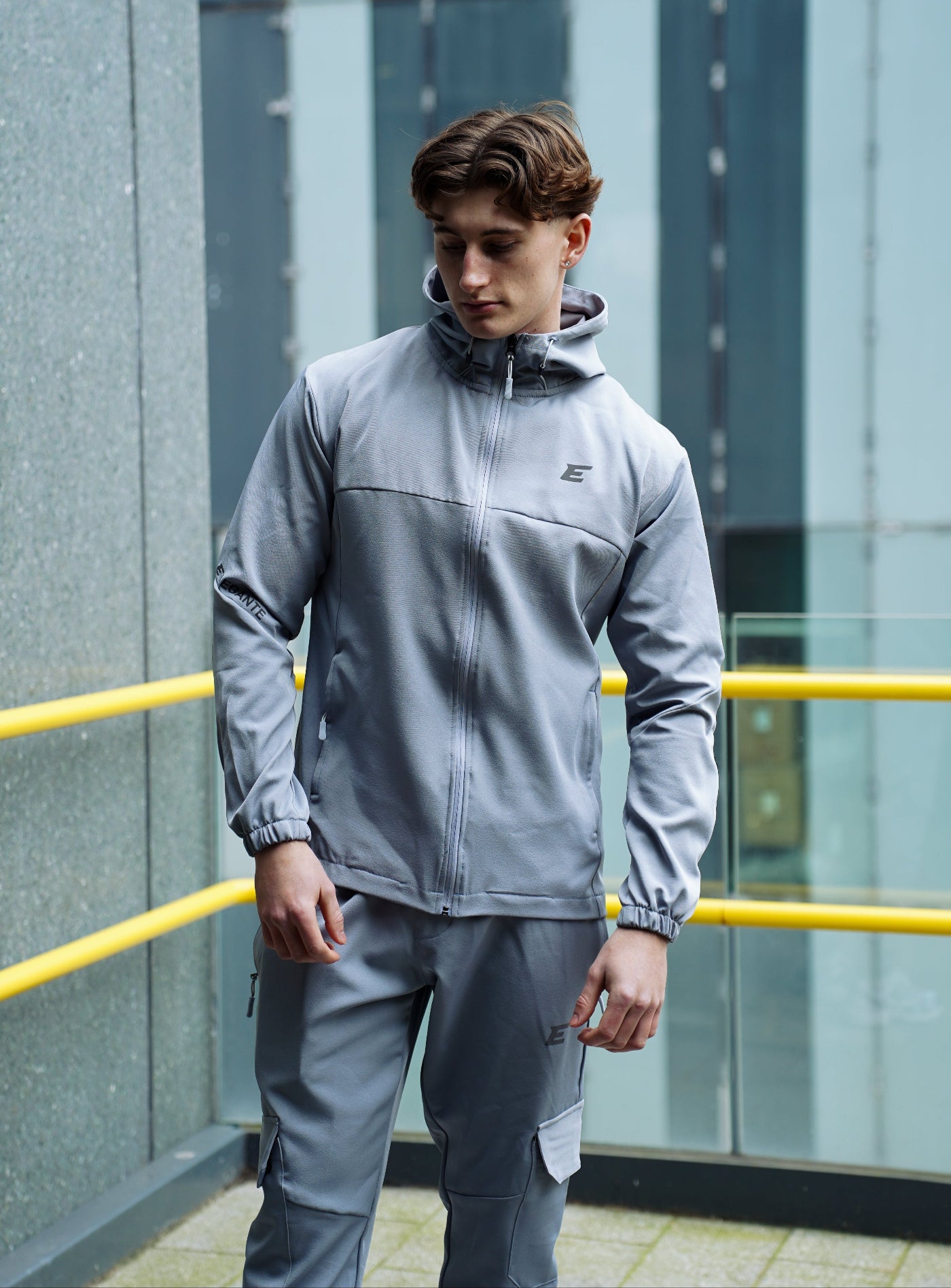 man wearing a gray tracksuit standing outside a building with a yellow railing.