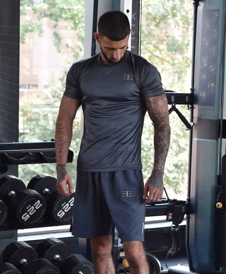 Man in athletic wear standing in a gym with weights and exercise equipment.