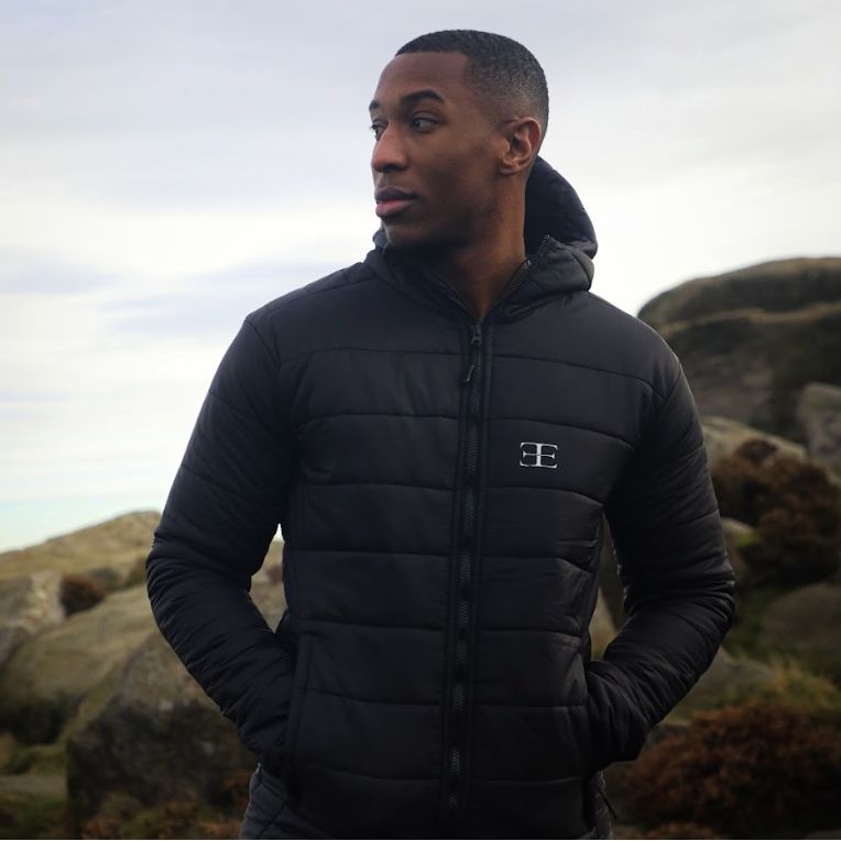 Man wearing a black puffer jacket with a logo in a natural setting