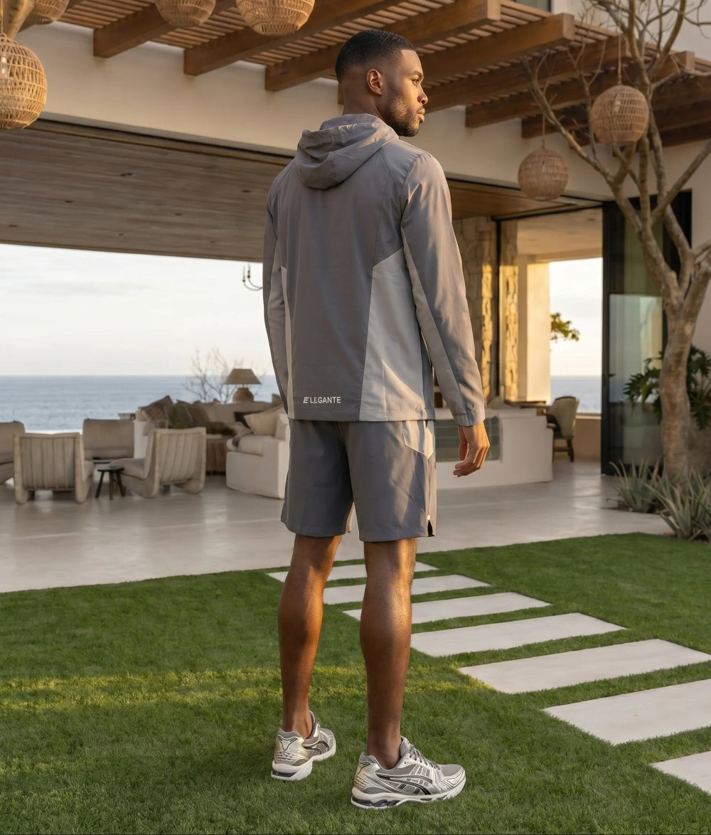 Man in athletic wear hooded jacket and matching shorts set standing on a patio 
