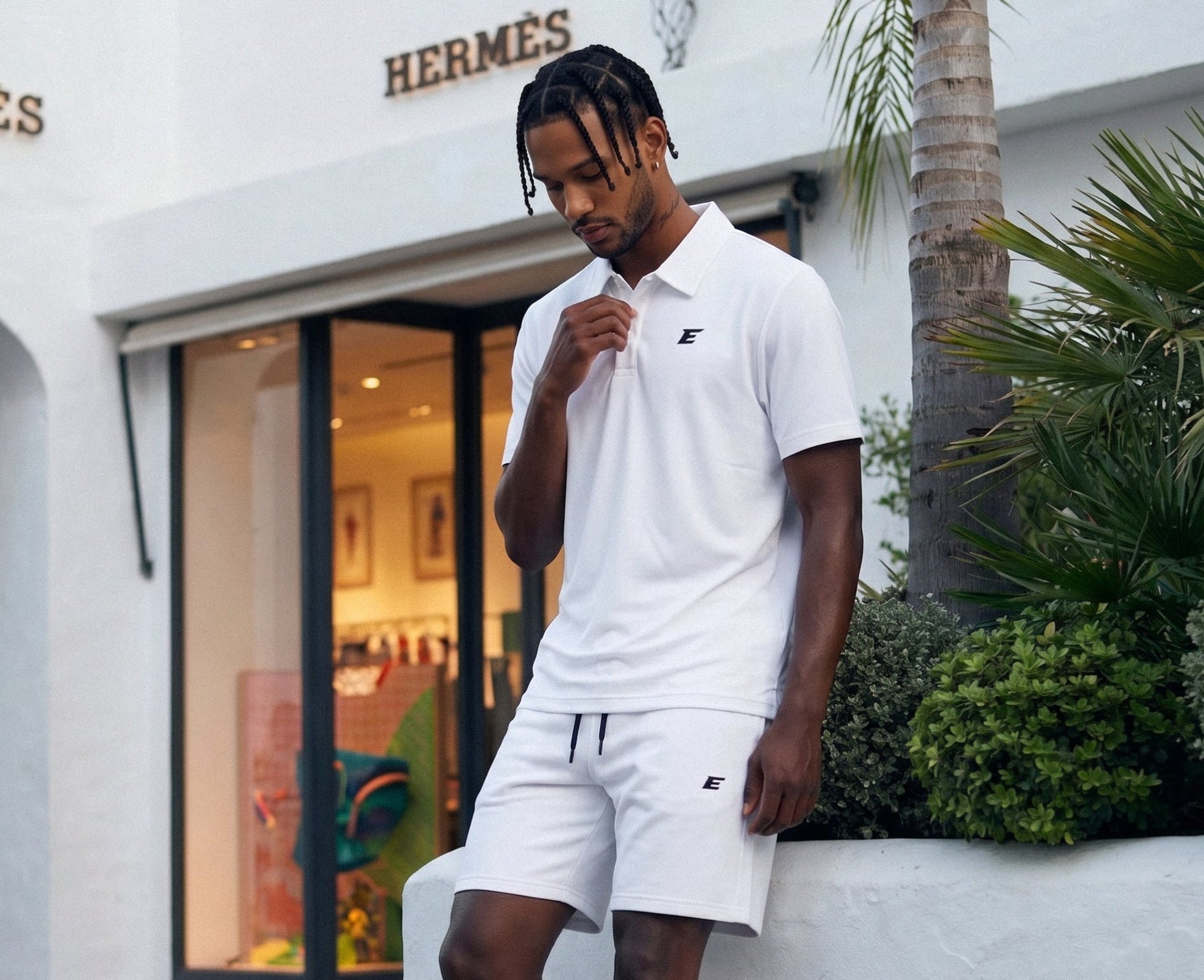 Man in white shhorts and tshirt set standing in front of a Hermes store