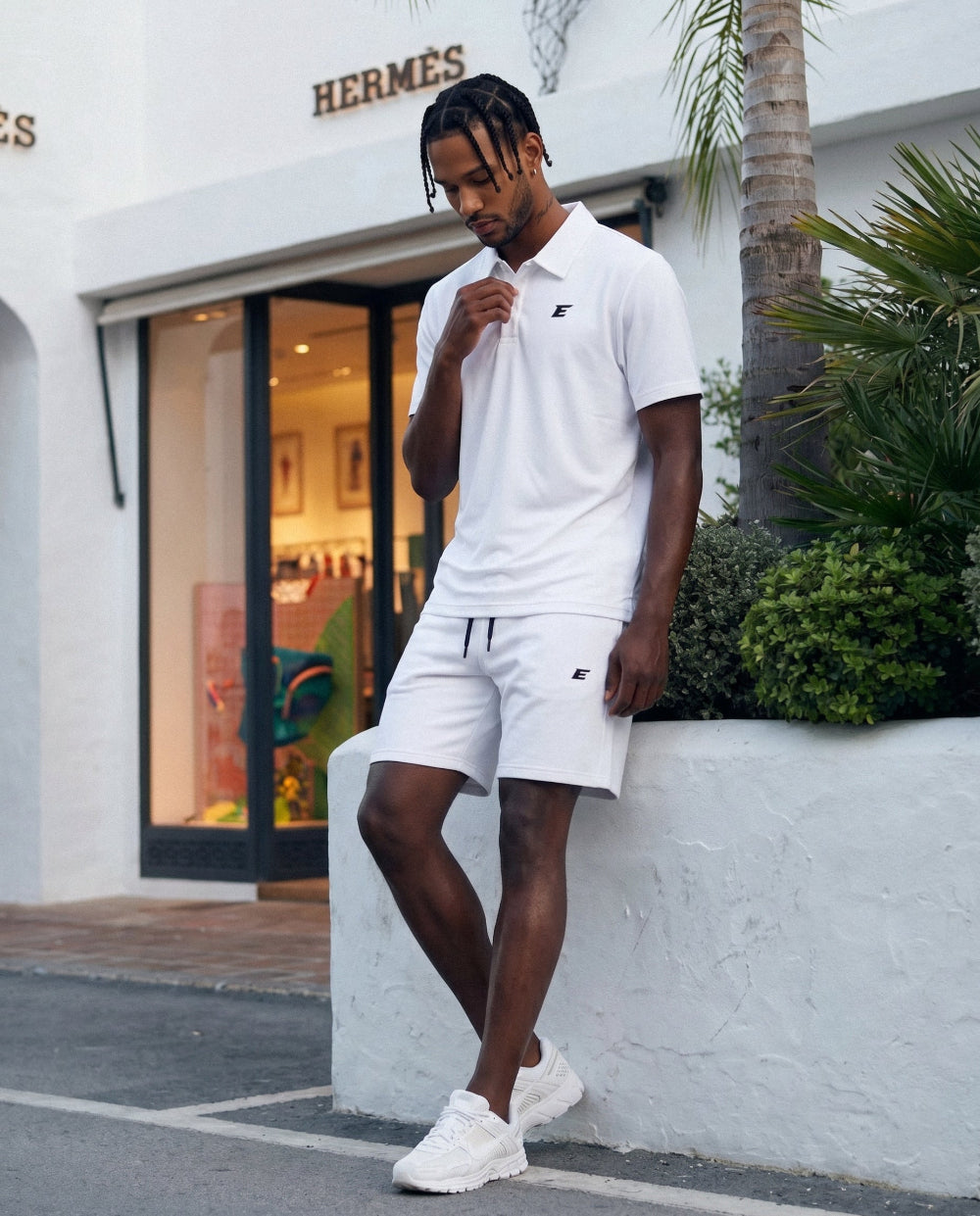 Man in white polo shit and short set outfit standing in front of a Hermes store