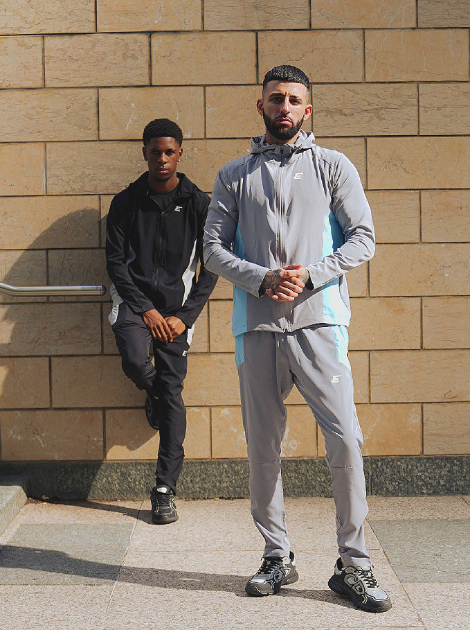 two men wearing activewear tracksuits sets, full black tracksuit and a man at the front wearing grey and blue tracksuit