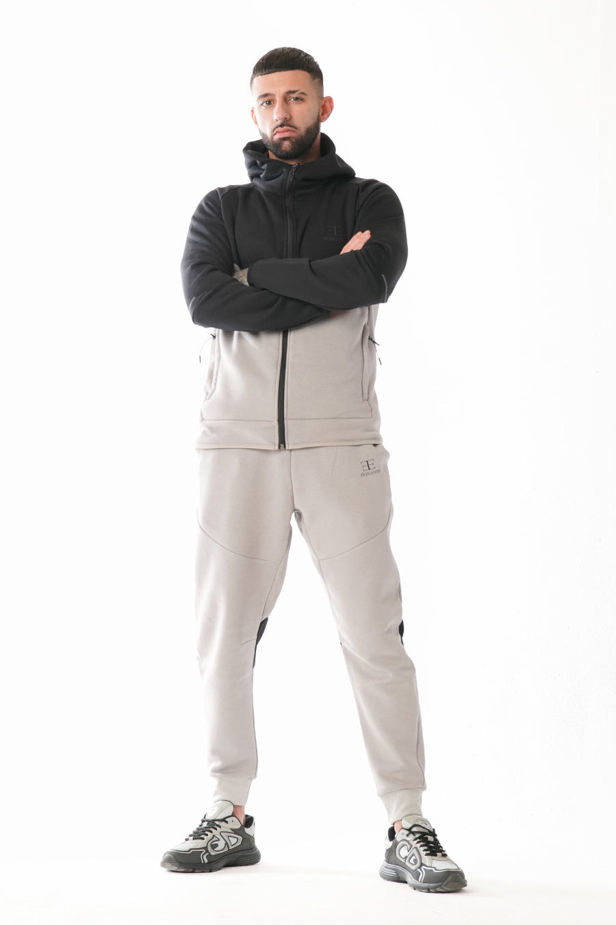 Man wearing light gray pants with black and grey hoodie on a white background