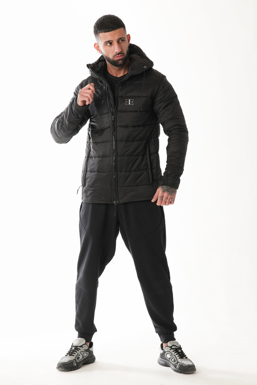 Man wearing a black puffer jacket and pants on a white background