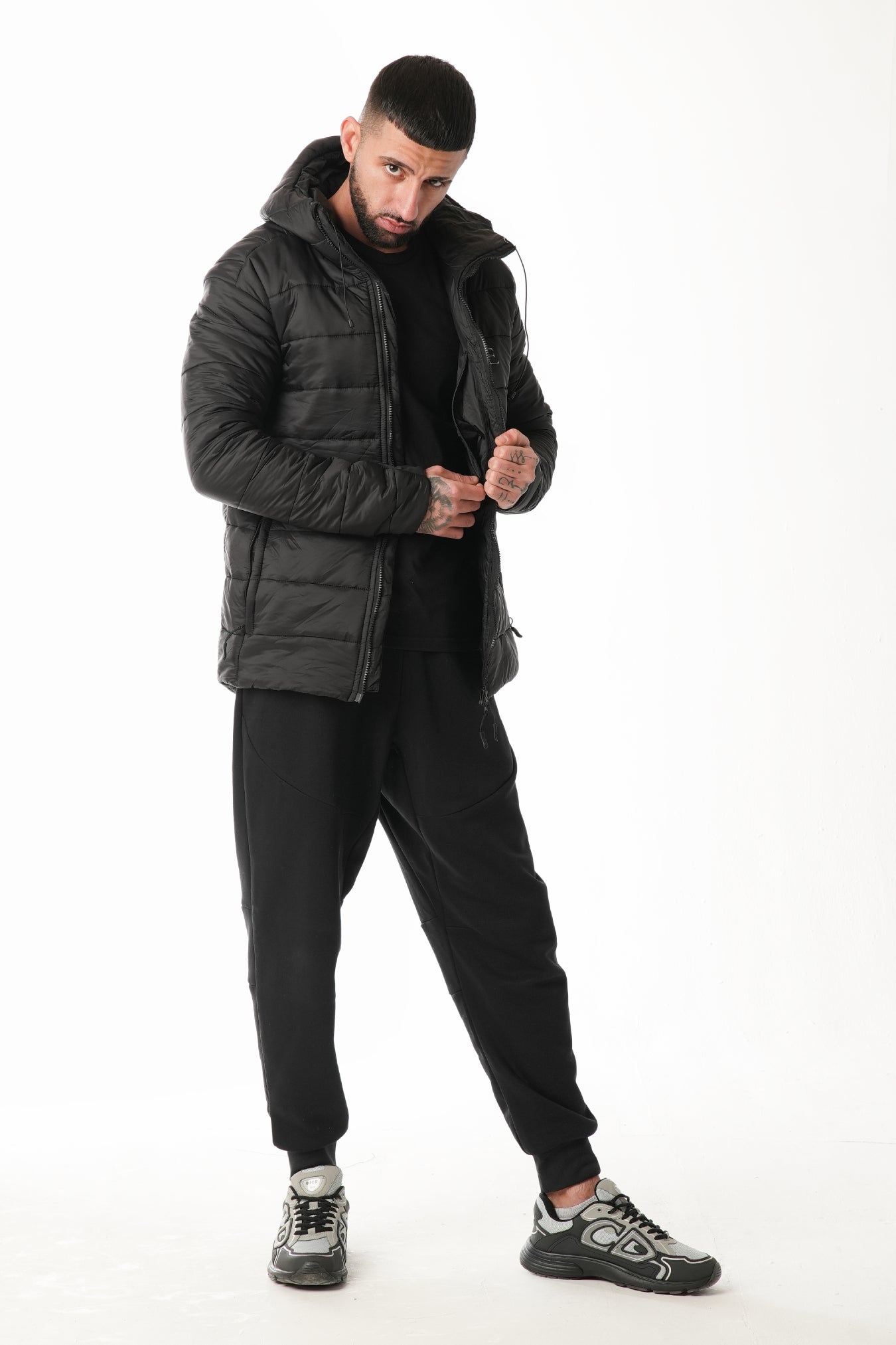 Man wearing a black puffer jacket and pants on a white background