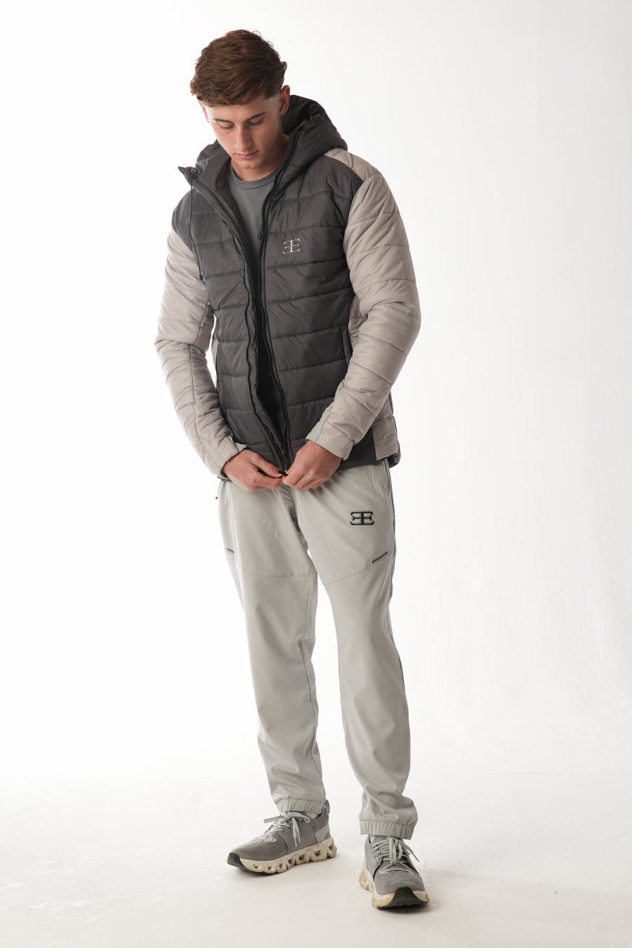 Man wearing a gray and black puffer elegante brand  vest over a gray hoodie and pants on a white background