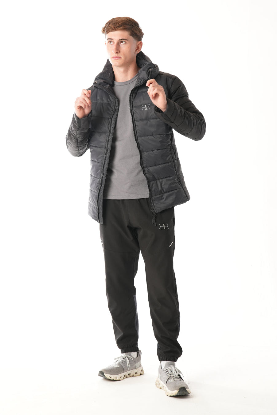 Man wearing a black puffer jacket over a gray t-shirt on a white background