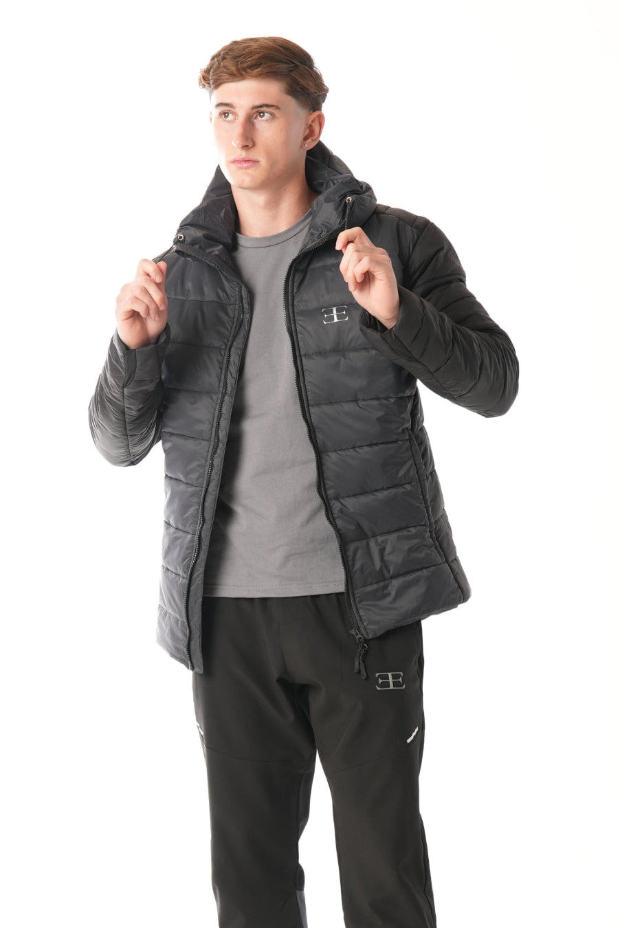 Man wearing a grey black puffer jacket over a gray t-shirt on a white background