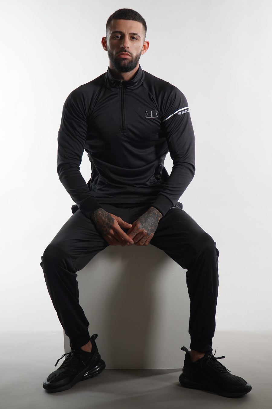 Man wearing a black athletic outfit with elegante logo on a white background