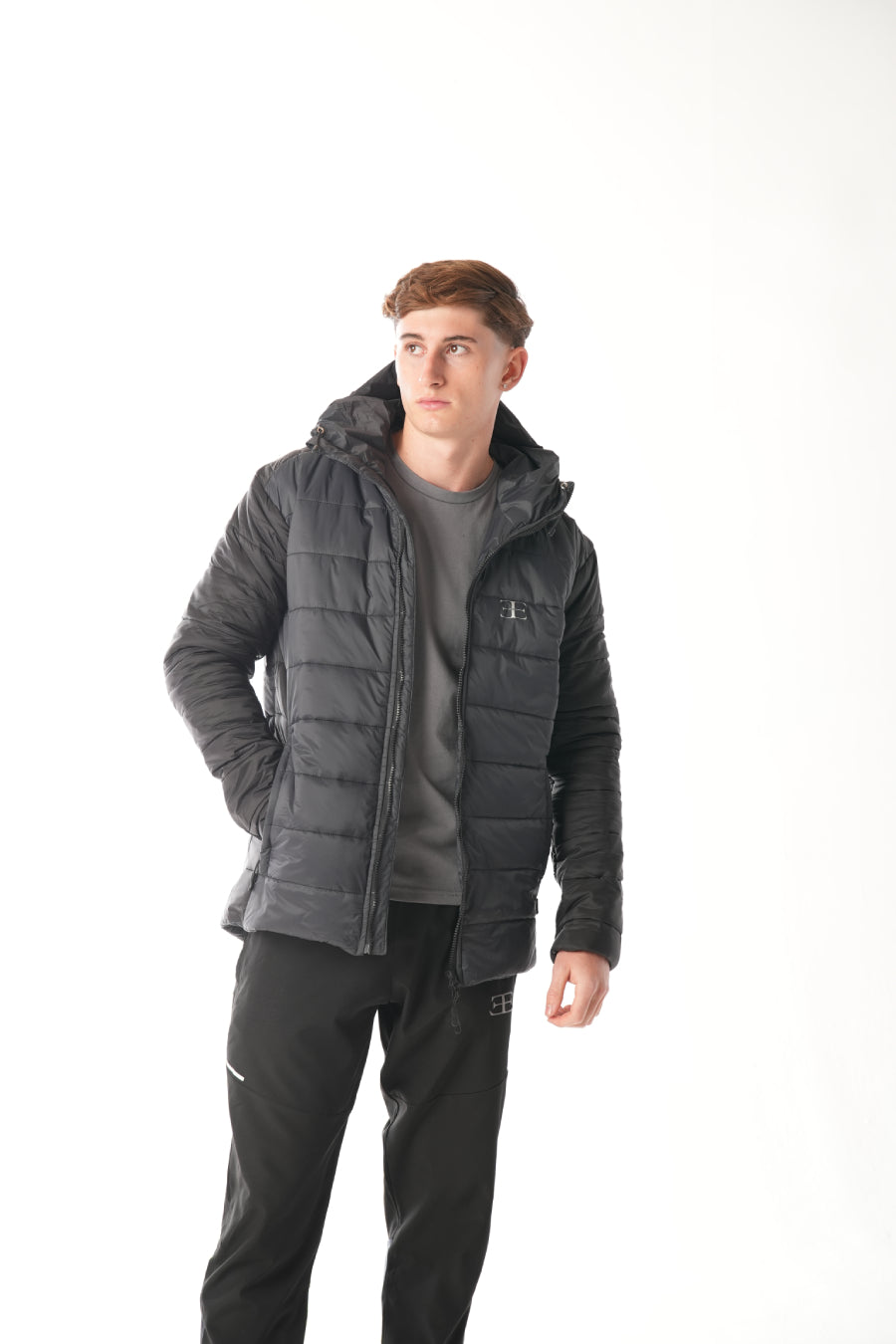 Man wearing a black puffer jacket over a gray t-shirt on a white background