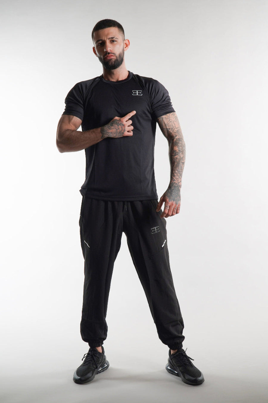 Man wearing a black t-shirt and tracksuit pants with elegante brand logo on a white background