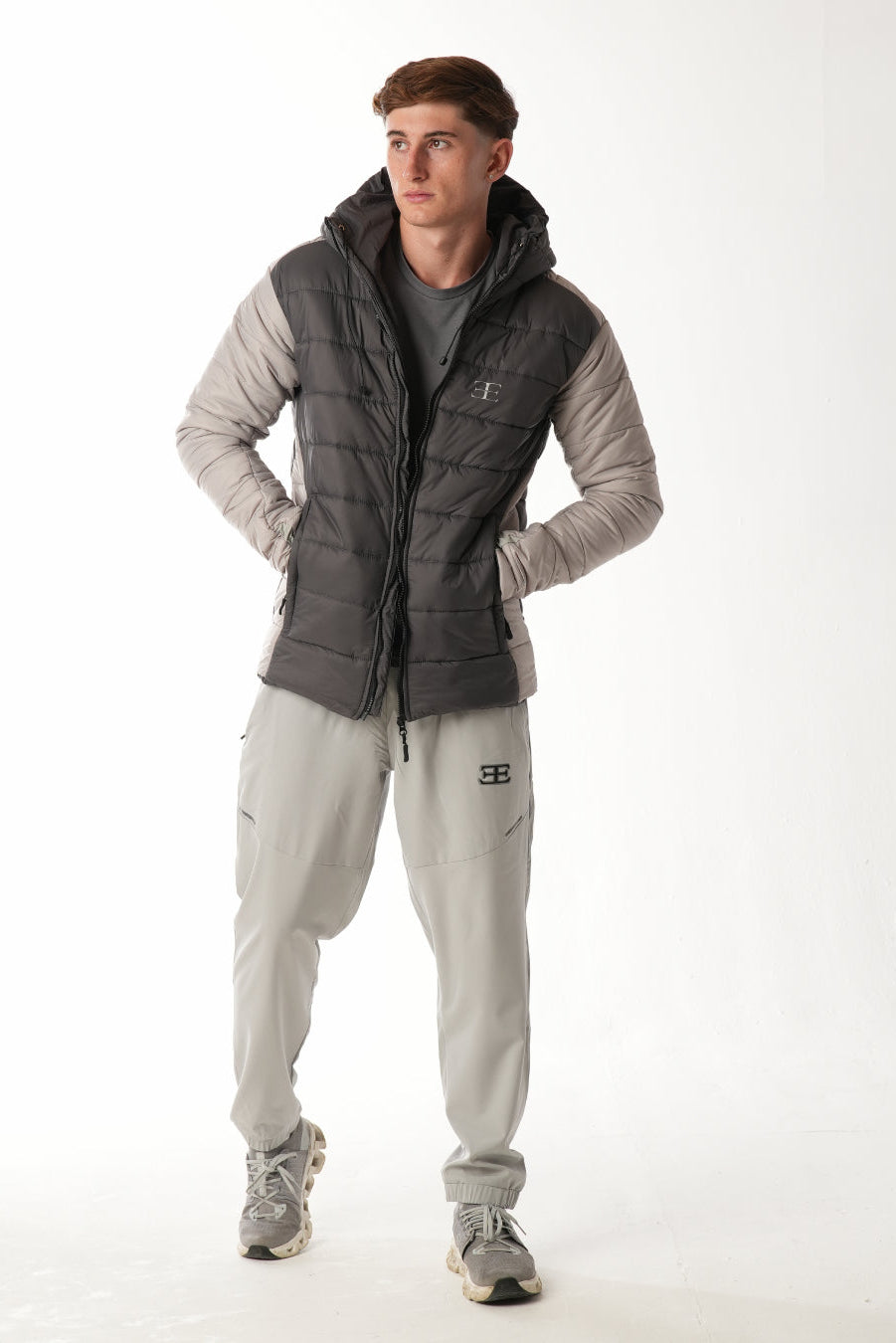 Man wearing a gray puffer jacket and grey pants on a white background