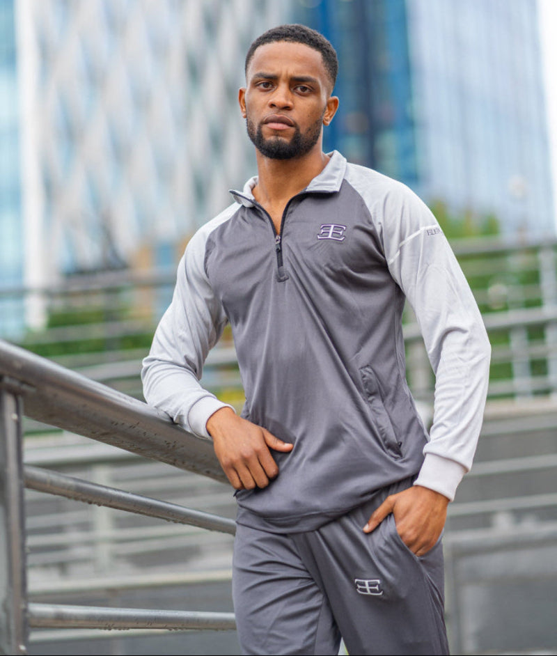 man wearing dark grey tracksuit and zip top worn by male black model with buildings in the background